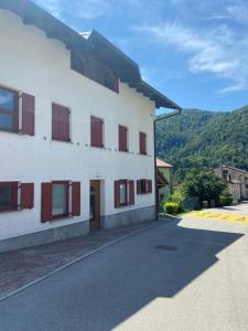 a white building with red shuttered windows on a street at Apartma SOČA in Most na Soči