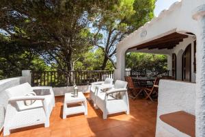 un patio con sillas blancas, mesa y árboles en Villa Menorca Ses Roques Vermelles by Mauter Villas, en Cala Morell