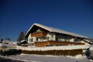 ein schneebedecktes Haus mit einem Auto davor in der Unterkunft Gästehaus Wiesenhof in Fischen im Allgäu
