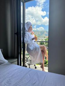 een vrouw in een badjas op een balkon met een drankje bij Hotel Pazari & Apartments in Korçë