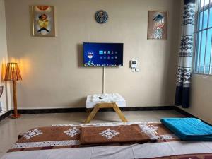 a living room with a table and a tv on the wall at Oak Cottage in Dar es Salaam