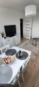 ein Wohnzimmer mit einem weißen Tisch mit Stühlen und einem TV in der Unterkunft Apartament Biała Przystań Stogi in Danzig