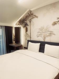 Uzunkum Hotel في طرابزون: سرير أبيض كبير في غرفة بها أشجار نخيل على الحائط