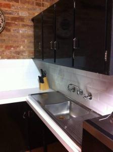 eine Küche mit einer Spüle aus Edelstahl und schwarzen Schränken in der Unterkunft The Coachhouse in Goulburn