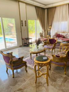 Lovely Villa 5- bedroom with Overflow Pool with Nice Garden at Green Oasis Resort في الإسكندرية: غرفة معيشة مع كراسي وطاولات وأريكة
