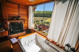 eine Badewanne in einem Zimmer mit einem großen Fenster in der Unterkunft Chalés Grecco in Venda Nova do Imigrante
