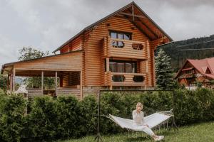 a woman sitting on a hammock in front of a log house at Айворі Хаус in Mykulychyn