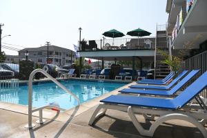 a pool with blue lounge chairs next to a building at Grecian Garden Motel in North Wildwood