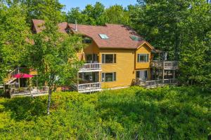 a large yellow house in the middle of trees at Elk Rapids Condo with Balcony Overlooking Elk Lake! in Elk Rapids