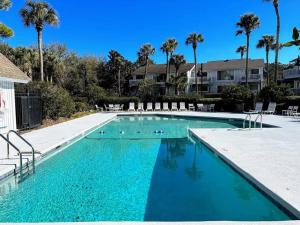 a large blue swimming pool with chairs and palm trees at Lagoon Villa 22 - Private Villa! Close Walk to Beach! in Isle of Palms