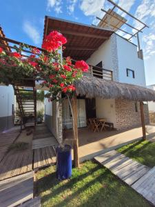 een villa met een rieten dak en rode bloemen op een terras bij Condomínio Shalom Beach in Canoa Quebrada