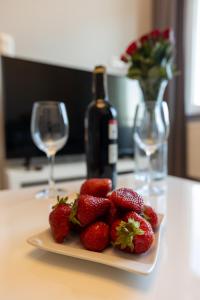 a plate of strawberries on a table with a bottle of wine at Ostróda City Center PKO lake apartments balcony in Ostróda