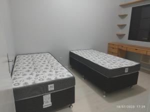 2 Einzelbetten in einem Zimmer mit einem Schreibtisch in der Unterkunft Quarto e piscina in Marechal Cândido Rondon