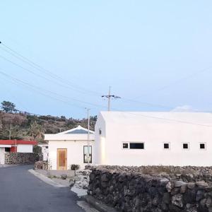 a white building with a stone wall next to a street at A shell in Jeju in Seogwipo