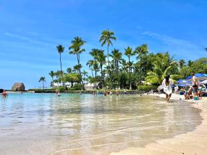 a beach with people in the water and palm trees at MaiLan Hale in Kailua-Kona