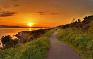 a person walking down a path with the sunset in the background at Seaview Apt in Buncrana with balcony in Buncrana