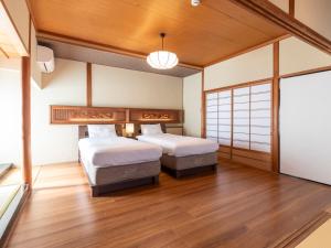 two beds in a room with wood floors and a window at Tabist Nanki Shirahama Ryokan Mantei in Shirahama