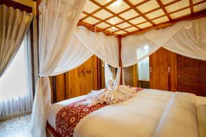 a bedroom with a large white bed with curtains at Kanchana Cottages in Uluwatu