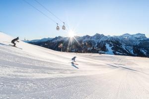2 personas esquiando por una pista cubierta de nieve con un remonte en Hotel Alp Cron Moarhof en Valdaora