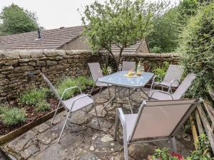 een patio met een tafel en stoelen en een stenen muur bij Ribble Cottage in Settle