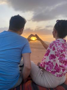 un hombre y una mujer sentados en la playa viendo la puesta de sol en Marina Wadi Rum Camp en Disah