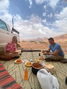 a man and woman sitting at a picnic table with food at Wadi Rum Spring Moon & Jeep Tour in Wadi Rum