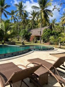 a resort swimming pool with two chairs and palm trees at The Papalagi Resort in Gili Gede