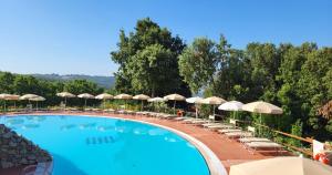 a large swimming pool with chairs and umbrellas at Resort Le Tegole in Riparbella
