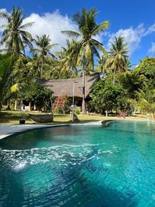 una piscina di fronte a una casa con palme di The Papalagi Resort a Gili Gede