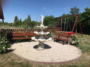 a fountain in a park with two benches and a swing at Tó-Party Apartman in Kiszombor