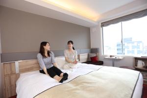 two women sitting on a bed in a hotel room at Urban Hotel Kyoto Gojo Premium in Kyoto