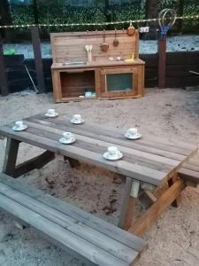 una mesa de picnic de madera con tazas y platillos. en le gite de zoelie en Chaineux