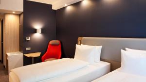ボーフムにあるHoliday Inn Express Bochum, an IHG Hotelのベッド2台と赤い椅子が備わるホテルルームです。