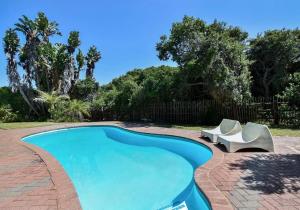 a swimming pool with two white chairs next to it at Dunes Cottage in Plettenberg Bay