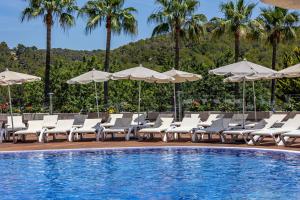 una piscina con tumbonas blancas y sombrillas junto a una piscina en Ona Palmira Paradise, en Paguera