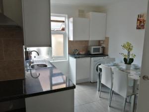 a kitchen with white cabinets and a table and chairs at Lovely 3 Bedrooms Flat Near Romford Station With Free Parking in Romford