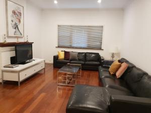 a living room with a black leather couch and a television at Leisurely Manor - spacious three bedroom home in Fremantle in Fremantle