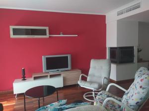 a living room with a red wall with a tv and chairs at Sol, mar y naturaleza in Pontevedra