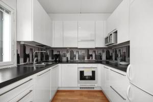 a white kitchen with white cabinets and black counter tops at Kotimaailma - Iso ja valoisa kaksio, Espoon Keskustassa in Espoo