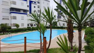 a swimming pool with two palm trees in front of a building at Appartement cosy à BOUZNIKA in Bouznika