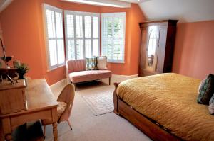 Schlafzimmer mit orangefarbenen Wänden, einem Bett und einem Stuhl in der Unterkunft Hazelhurst Farm in Sway