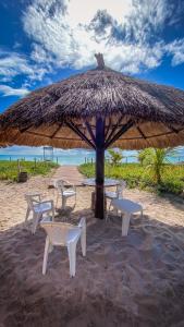 uma mesa e cadeiras debaixo de um guarda-sol de palha na praia em Village Miramar em Maragogi