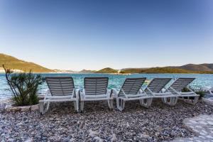 three chairs sitting on the beach next to the water at Apartments Krstičević in Klek