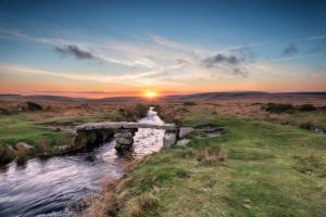 a bridge over a river with the sunset in the background at Modern, self-contained annexe in the countryside in Callington