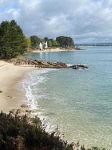 a beach with the ocean and a house in the distance at Taïcyté Beg Meil in Fouesnant