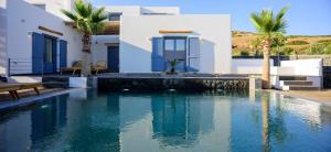 a swimming pool in front of a house with palm trees at White Dream Suites Antiparos in Antiparos
