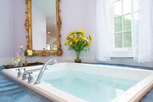 uma banheira com um espelho e um vaso de flores em The Villa Bed and Breakfast em Westerly
