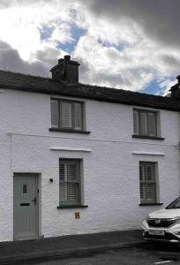 a white house with windows and a car parked in front at Cosy Lake District Cottage in Staveley