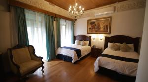 a bedroom with two beds and a chair and a chandelier at Hotel Luna in Guanajuato