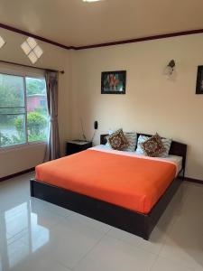 ein Schlafzimmer mit einem Bett mit orangefarbener Bettwäsche und einem Fenster in der Unterkunft ธนวรรณรีสอร์ท - Thanawan Resort in Ban Phra Trong